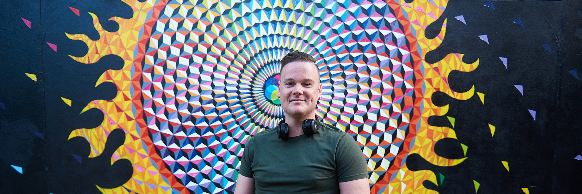 Damon sitting in front of a piece of colourful street art, looking to camera.