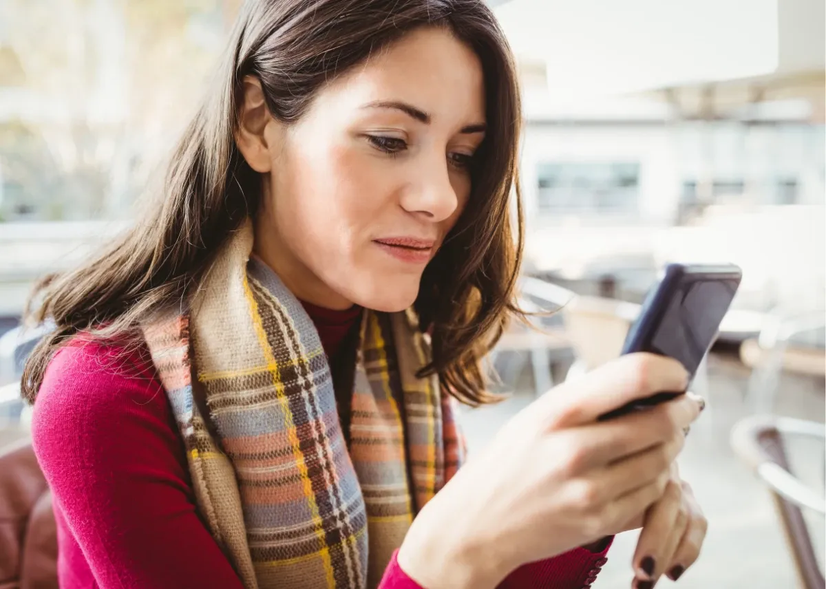 Caucasian woman in her early 40s, sitting in an outdoor cafe, browsing the Forums on her smartphone