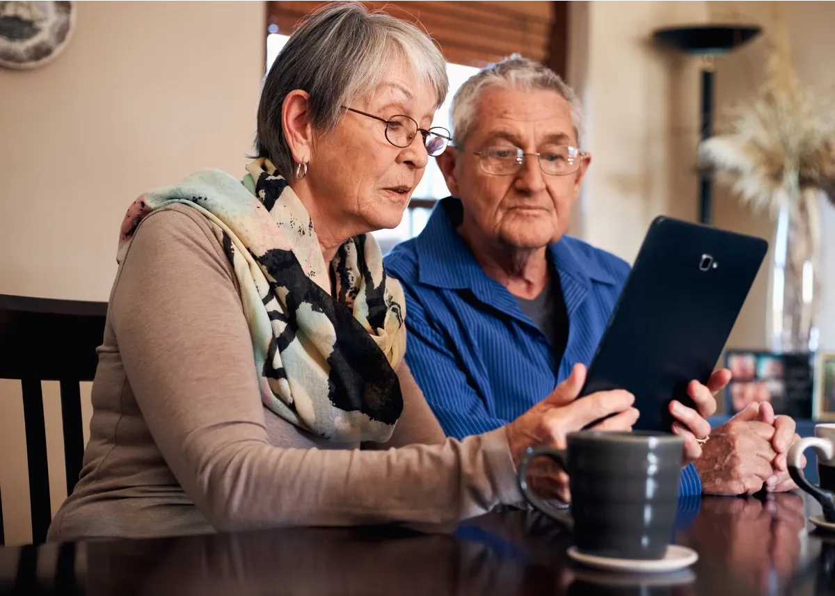 Grandparents sitting at a dining table and using a tablet to access SANE Forums and connect with other carers and family members